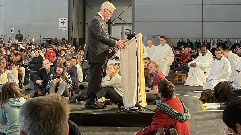 Bundespräsident a.D. Joachim Gauck steht am Rednerpult inmitten der Teilnehmer des Mittagsgebets